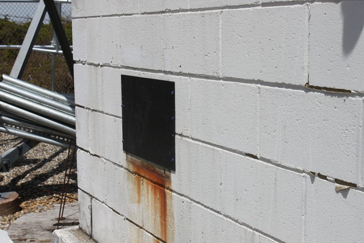 Hole in cinder block building covered with aluminum rack panel blank